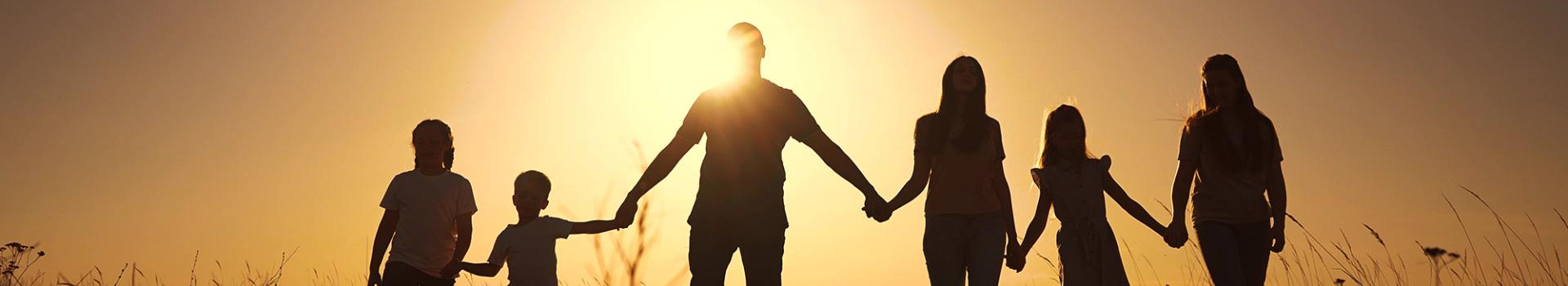 Family holding hands with sun setting behind them